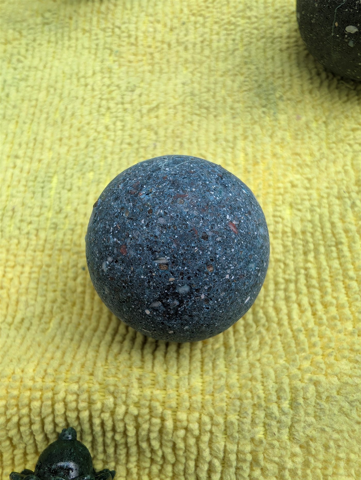 A deep slate-blue memorial pearl, hand-polished, its surface flecked with the natural white crystals of the cremains it is made from.